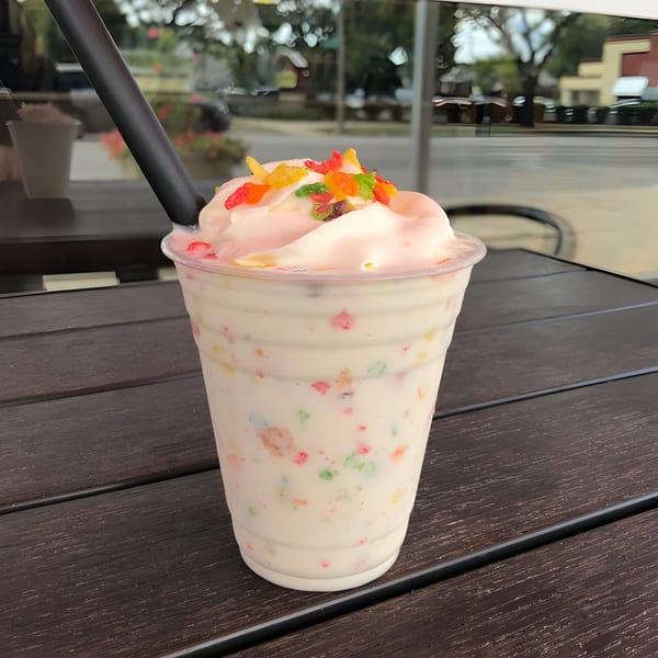 A Burger MOOvment milkshake with whipped cream and colorful candy sits on a wooden table.