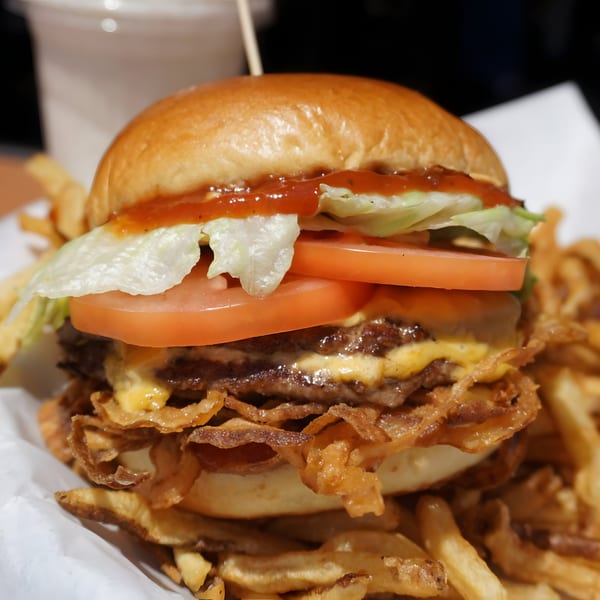 A double cheeseburger with lettuce, tomato, sauce, and crispy fried onions, served with fries.