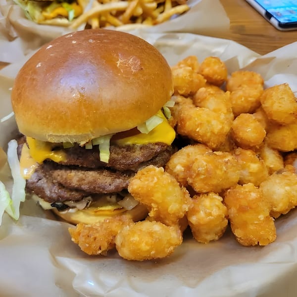 A double cheeseburger with melted cheese, lettuce, and sauce, served with a side of golden tater tots.