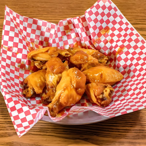 Sweet and sticky chicken wings in a red and white checkered paper-lined basket.