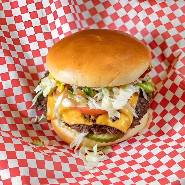 A Burger MOOvment cheeseburger with lettuce, tomato, and pickles, wrapped in red and white checkered paper.